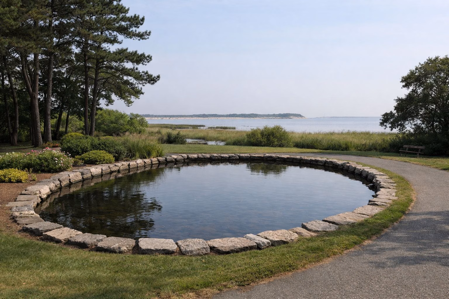 A small pond in a village park with lawn, flower beds and shade trees