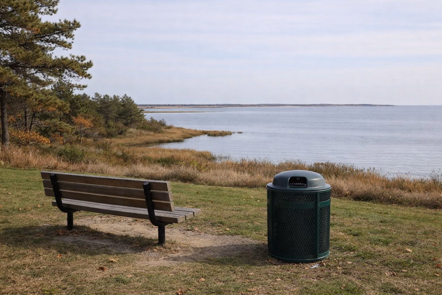 A wooden bench and trash receptacle overlooking a calm bay